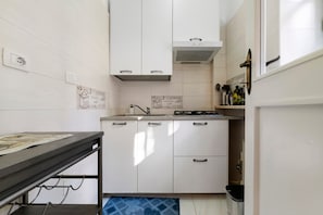 A compact kitchen with white cabinets, a stainless steel countertop, and a gas stove.
