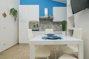 Una cucina moderna con mobili bianchi, una parete d'accento blu e un tavolo da pranzo apparecchiato per due.
