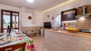 A modern kitchen with a central island, a dining area with a floral tablecloth, and a view through a window. - Villa "Casa Vacanza Errante" with Sea View, Pool & Wi-Fi (menfi)