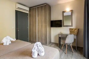 A hotel room with a bed, a desk, a chair, a TV, and a wardrobe.
