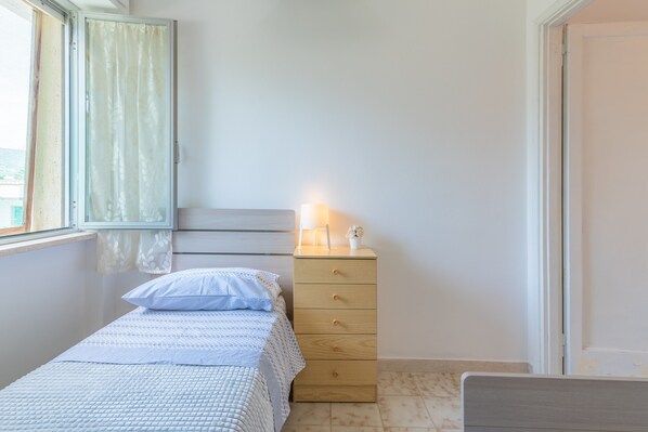 Een slaapkamer met een bed, een houten dressoir, een raam met gordijnen en een bedlamp.