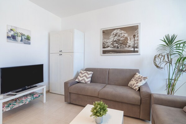 A living room with a flat-screen TV, a sofa, a coffee table with a plant, and a cabinet.