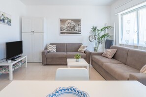A modern living room with a sofa, a coffee table, a TV on a stand, and a window with heart-patterned curtains.