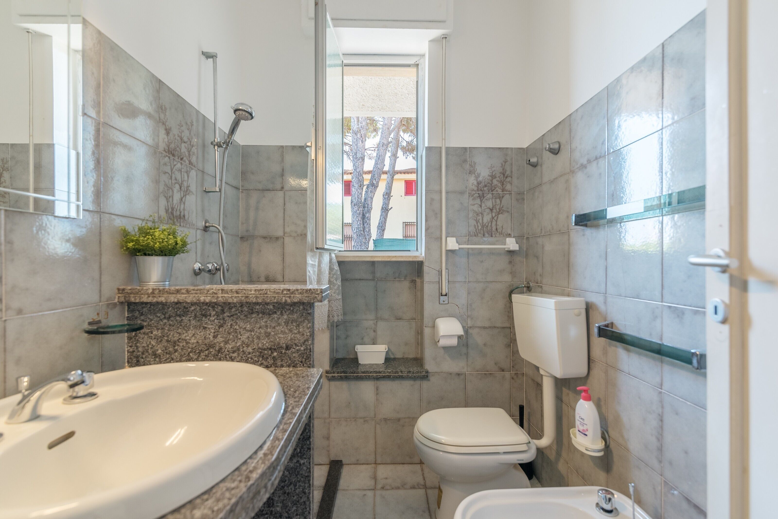 A bathroom with a large sink, toilet, and shower. There is a window providing natural light.