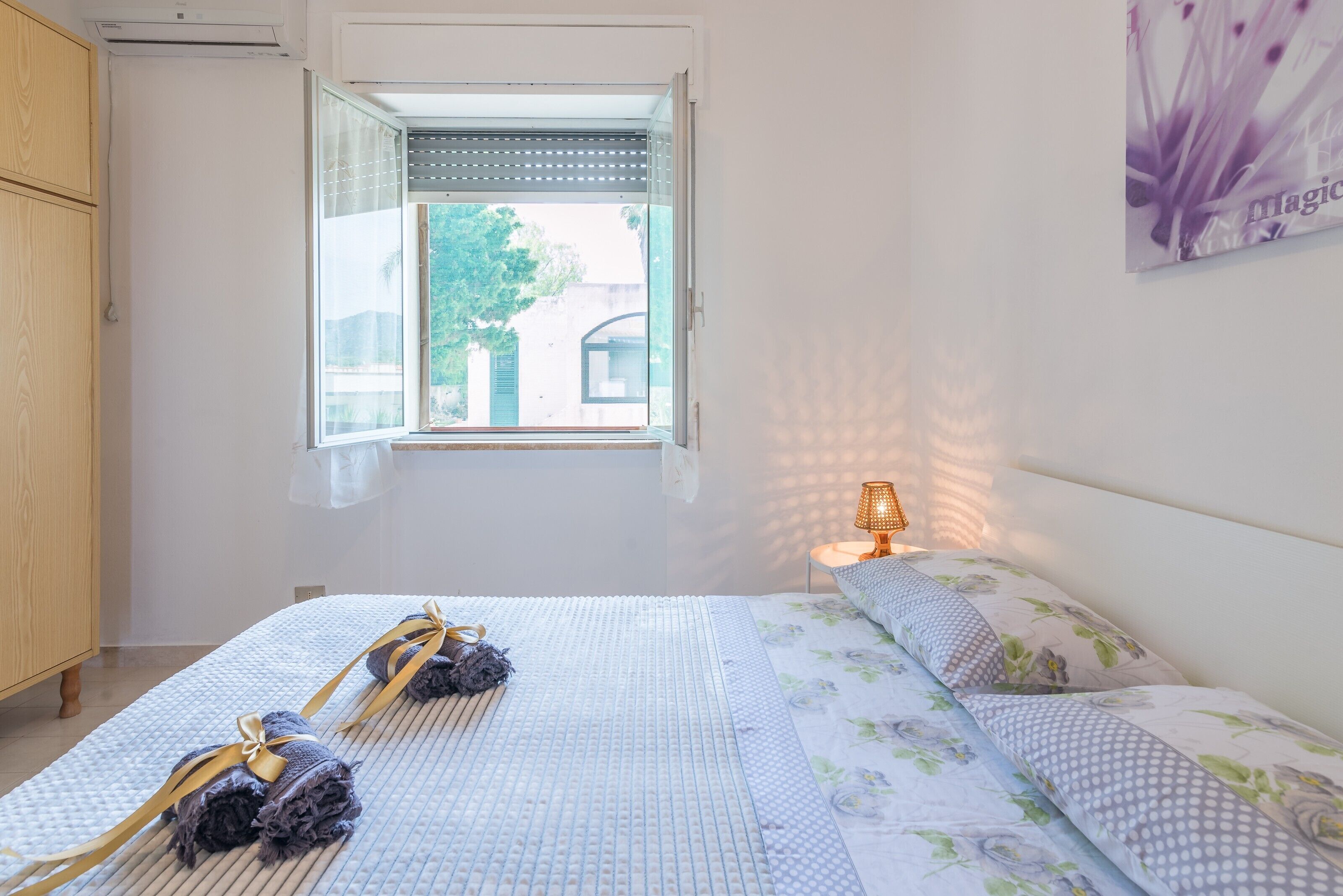 Une chambre à coucher avec un lit, une fenêtre, une lampe de chevet et un tableau accroché au mur.