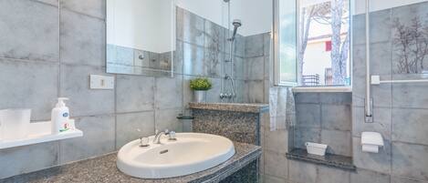 A modern bathroom with a granite countertop, a white sink, a handheld showerhead, and a toilet.
