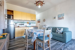 A compact kitchen with modern appliances, a dining table with chairs, and a teal sofa in a bright living area.