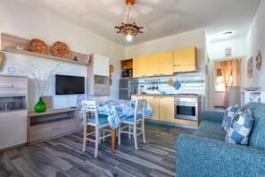 A modern kitchen with yellow cabinets, a dining area with a table and chairs, a sofa, and a TV mounted on the wall.