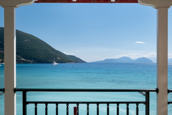 A coastal view with a balcony railing, clear blue sea, and distant mountains.