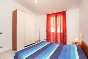 Une chambre à coucher avec un lit, une armoire, une table de chevet et une fenêtre avec des rideaux.
