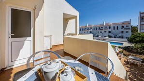 A balcony with a table set for breakfast, a pool in the background, and a building with a white facade. - Apartment Villas Brites nº4 with Shared Pool, Shared Garden, Balcony & Wi-Fi (Burgau)