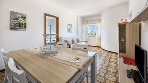 A room with a dining table, chairs, a sofa, a TV, and a window with curtains. - Apartment Villas Brites nº4 with Shared Pool, Shared Garden, Balcony & Wi-Fi (Burgau)