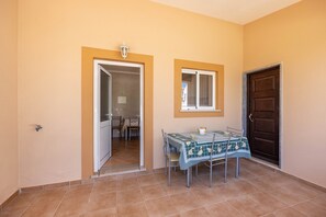 Une pièce comprenant une table à manger, des chaises, une fenêtre avec des stores, une porte et un luminaire.