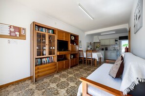A living room with a sofa, a wooden cabinet with glass doors, a dining area with a table and chairs, and a kitchen in the background.