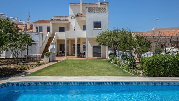 A two-story building with a swimming pool in the foreground, a well-maintained lawn, and a clear blue sky. - Holiday Home Villas Brites nº5 with Open Terrace, Shared Pool & Wi-Fi (Burgau)