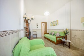 A bedroom with a green sofa, a wooden bed, a small table with a vase, and a mirror on the wall.