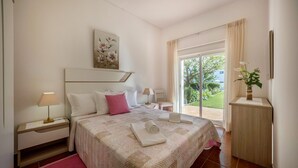 Un dormitorio con cama, mesitas de noche, cortinas y vistas a espacios verdes.