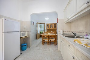 A compact kitchen with a refrigerator, microwave, wooden dining table, and a sink.