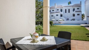 Un patio con una mesa dispuesta para tomar té, un edificio blanco al fondo y una piscina.