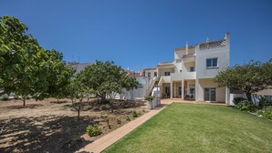 Edificio residencial de dos pisos con un césped cuidado, zona de estar al aire libre y árboles maduros.