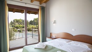 Een hotelkamer met een bed, een nachtkastje, een raam met gordijnen en uitzicht op een zwembad en groen buiten.