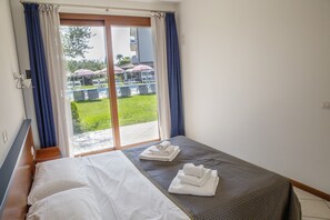 A hotel room with a bed, a window with curtains, and a view of an outdoor area with umbrellas.