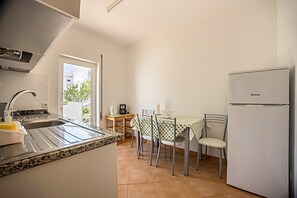 A kitchen with a sink, stove, and refrigerator, a dining table with chairs, and a window with a view of buildings.