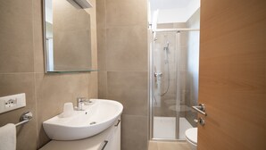 A modern bathroom with a glass-enclosed shower, a white sink, and a mirror above the sink. - Junior Suite 2 with Shared Pool & Balcony (Manerba del Garda)