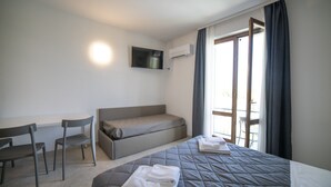 A modern hotel room with a bed, a sofa, a desk, and a TV. - Junior Suite 2 with Shared Pool & Balcony (Manerba del Garda)