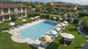 A rectangular swimming pool with lounge chairs and umbrellas, surrounded by well-maintained lawns and residential buildings. - Junior Suite 2 with Shared Pool & Balcony (Manerba del Garda)