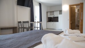 Ett hotellrum med en säng, ett skrivbord, stolar, ett litet kök och en dusch.