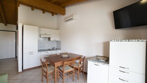 Une cuisine avec une table et des chaises en bois, des armoires blanches, un pare-feu en carreaux et un téléviseur fixé au mur.
