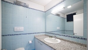 Une salle de bain avec des toilettes blanches, un lavabo doté d’un plan de travail en granit et un miroir au-dessus du lavabo.