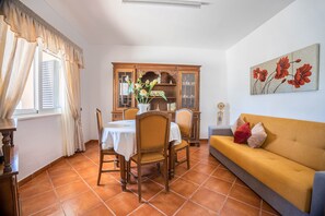 A dining area with a table and chairs, a sofa, a cabinet, and a painting on the wall.