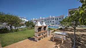 Eine Terrasse mit Grill, Pool und einem Gebäude mit weißen Wänden und roten Dächern.