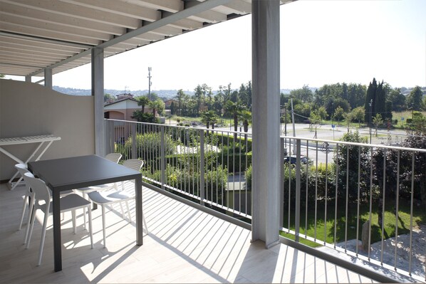 Un balcón con mesa y sillas, con vistas a una calle y vegetación.