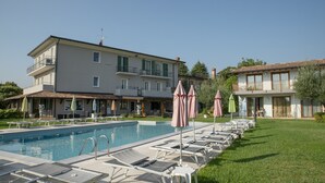 A swimming pool with lounge chairs and umbrellas, a building with balconies, and a well-maintained lawn. - Junior Suite 5 with Shared Pool and Private Balcony (Manerba del Garda)