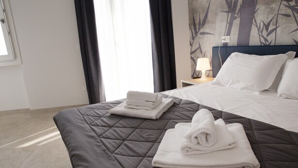 A hotel room with a bed, a nightstand with a lamp, and a wall with a bamboo pattern. - Deluxe Suite 3 with Shared Pool and Private Balcony (Manerba del Garda)