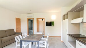 A modern kitchen with white cabinets, a dining table with chairs, a sofa, and a flat-screen TV mounted on the wall. - Deluxe Suite 3 with Shared Pool and Private Balcony (Manerba del Garda)