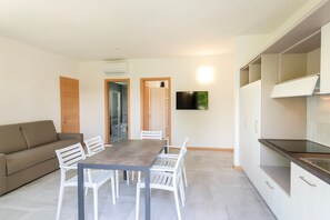 Eine moderne Küche mit weißen Schränken, einem Esstisch mit Stühlen, einer Couch und einem an der Wand befestigten Flachbildfernseher.