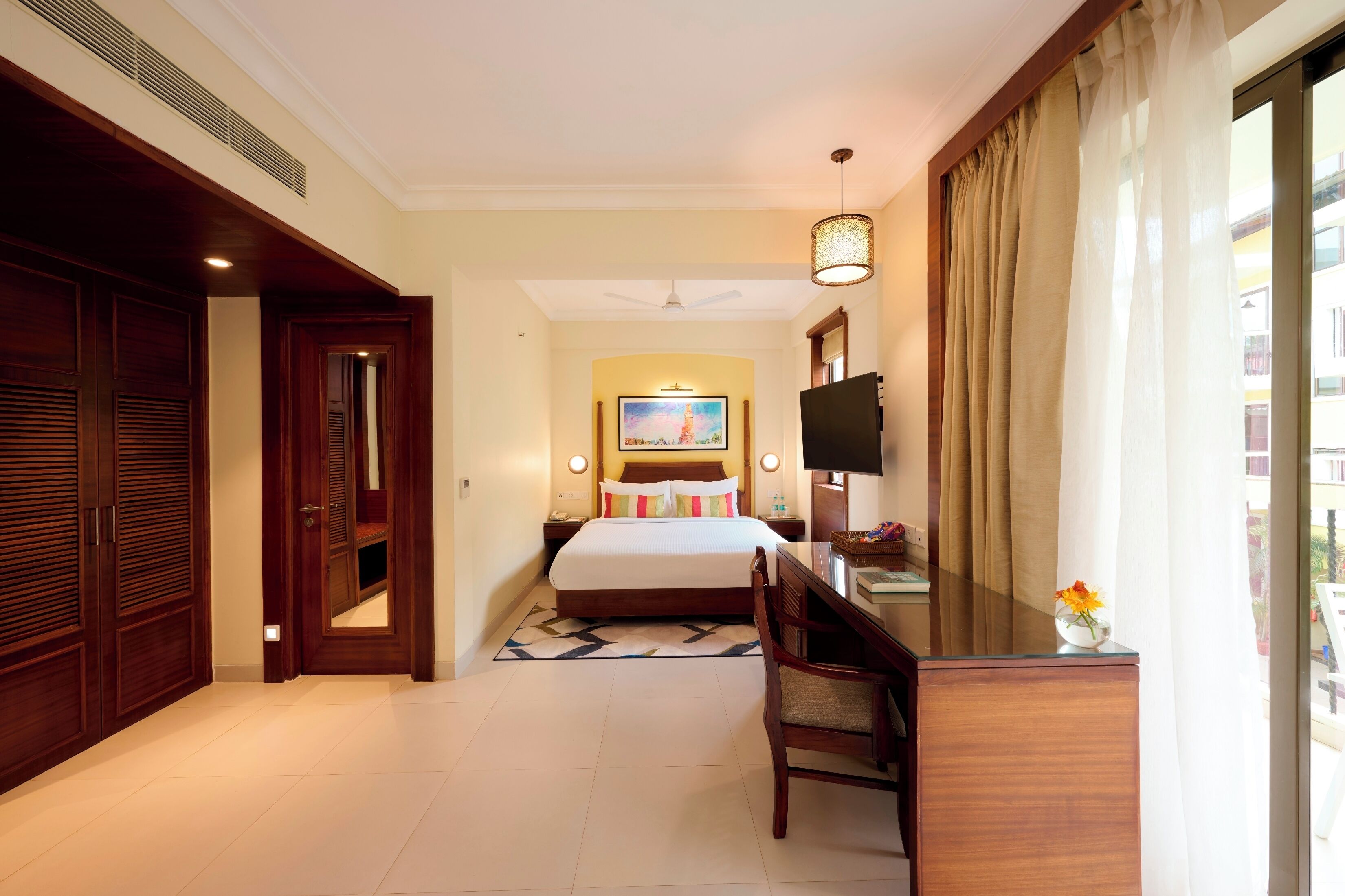 A hotel room with a bed, desk, chair, TV, and a view of the outside.