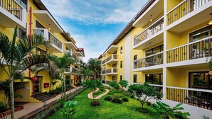 Un patio de hotel con un camino central, rodeado de exuberante vegetación y varios balcones.