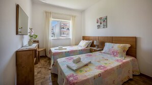 Camera d'albergo con due letti, una scrivania, una sedia, una finestra con tende e uno specchio.
