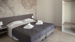 Un lit bien fait, avec une couverture grise, des oreillers blancs et des serviettes pliées posées sur le lit.