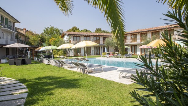 A pool area with lounge chairs and umbrellas, surrounded by buildings with balconies. - Suite 2 with Shared Pool and Private Balcony (Manerba del Garda)