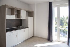 Une cuisine moderne avec des meubles blancs, un plan de travail noir et une porte-fenêtre coulissante donnant sur un balcon.