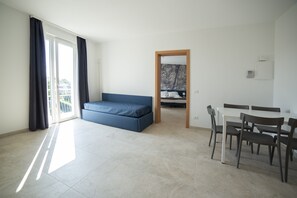Une pièce spacieuse avec un canapé bleu, une table à manger et des chaises, et une vue sur l’extérieur par une porte.