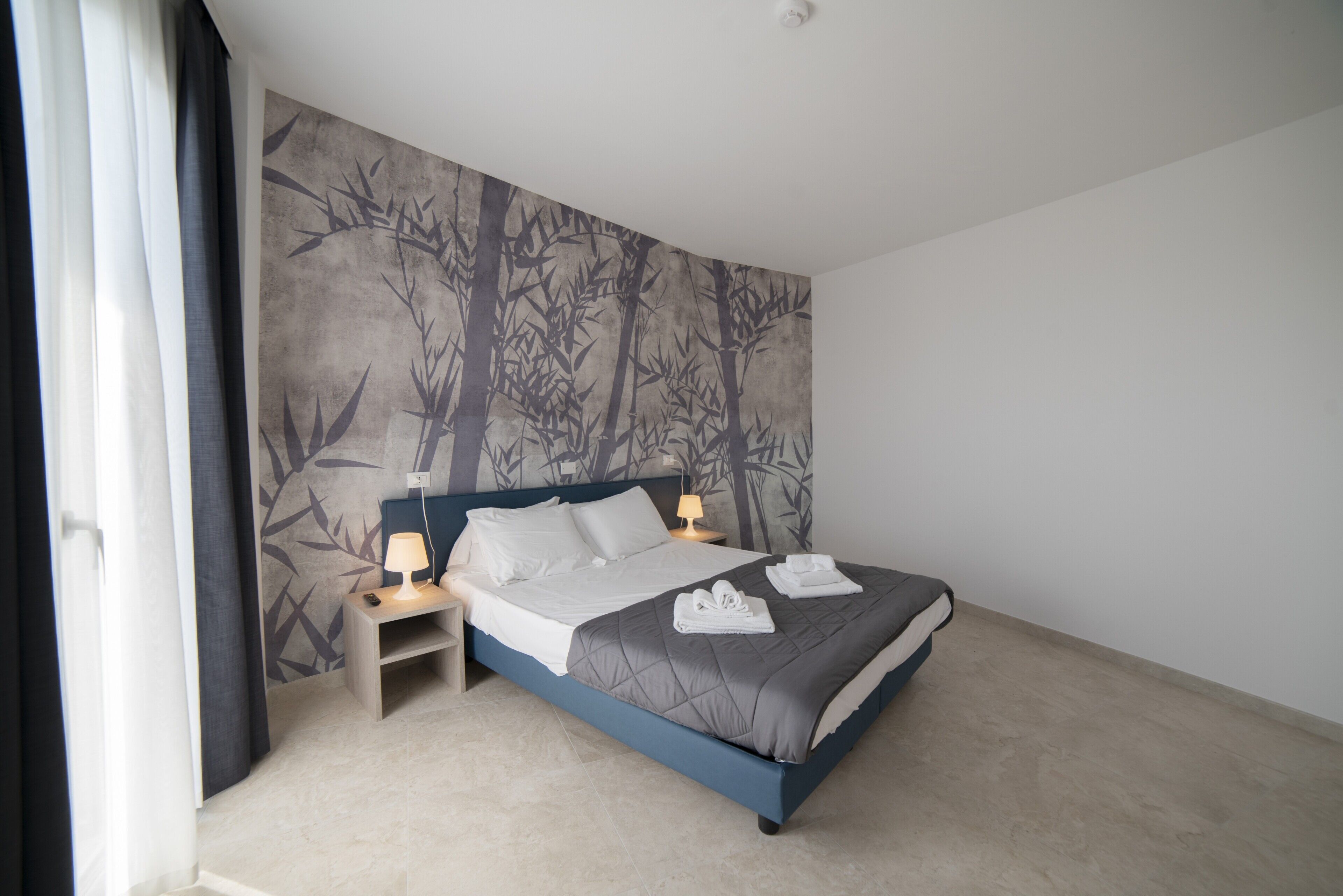 Une chambre à coucher avec un lit, des tables de chevet, une fresque murale et une fenêtre avec des rideaux.