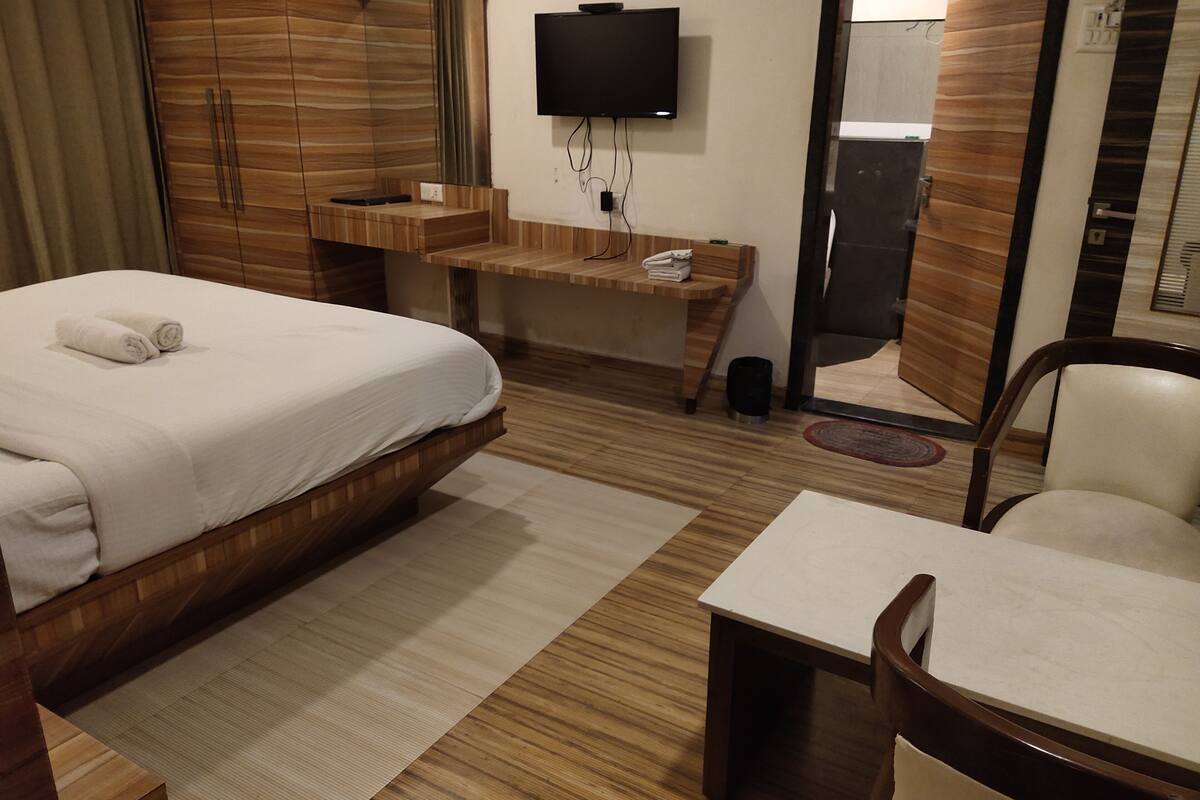 A hotel room with a bed, a desk, a chair, a TV, and a mirror.