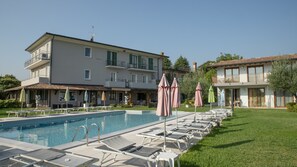 A poolside area with lounge chairs and umbrellas, a building with balconies, and a clear sky.